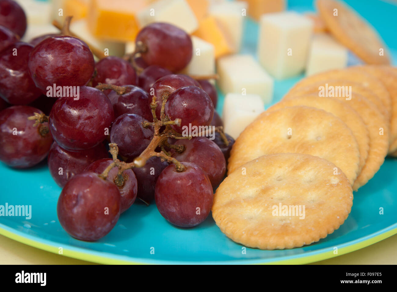 Frische rote Trauben setz Würfel verschiedene Käse und Cracker auf einem Teller blau und grün Stockfoto