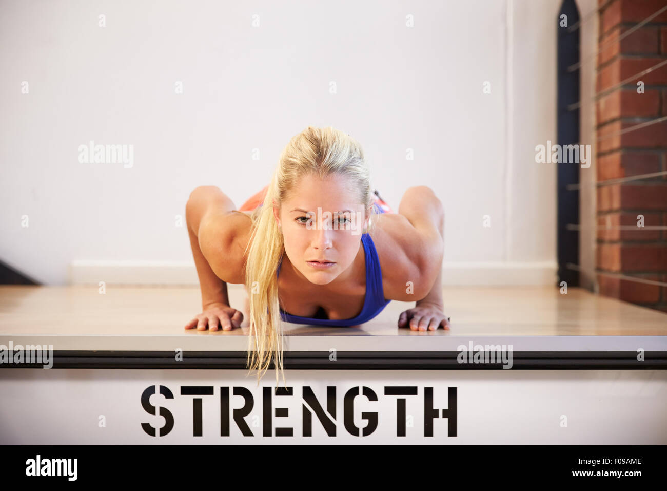Frau im Fitness-Studio macht Liegestütze auf Schritt mit der Bezeichnung Stärke Stockfoto