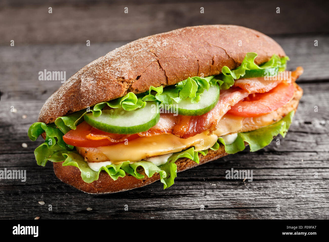 Sandwich mit Huhn, Speck, Käse und Gemüse auf einem rustikalen Hintergrund Stockfoto