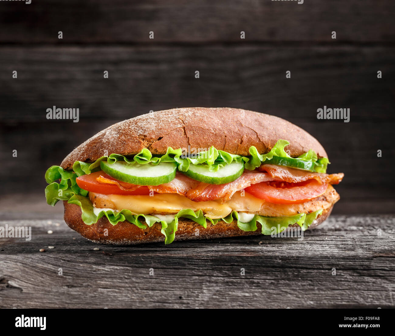 Sandwich mit Huhn, Speck, Käse und Gemüse auf einem rustikalen Hintergrund Stockfoto