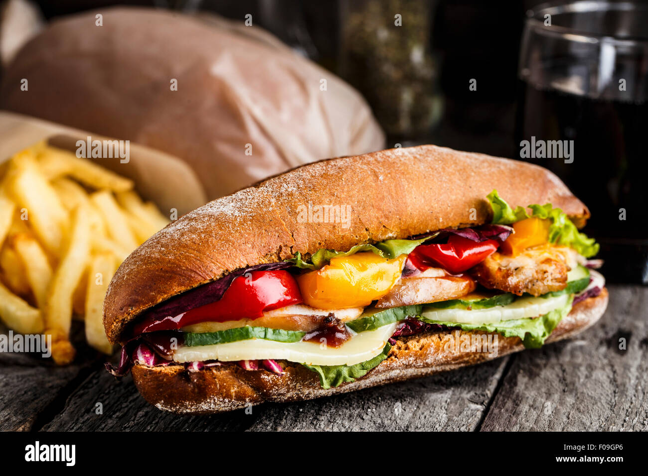 Sandwich mit Huhn, Pommes Frites und Glas Soda auf einem rustikalen Tisch Stockfoto