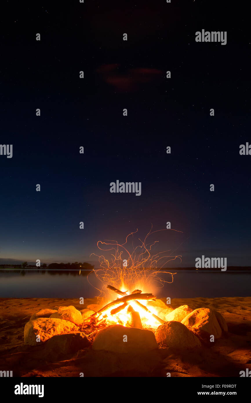 Funkenbildung Lagerfeuer am See unter dem Sternenhimmel.  Leichtes Glühen vom Sonnenuntergang am Horizont. Stockfoto