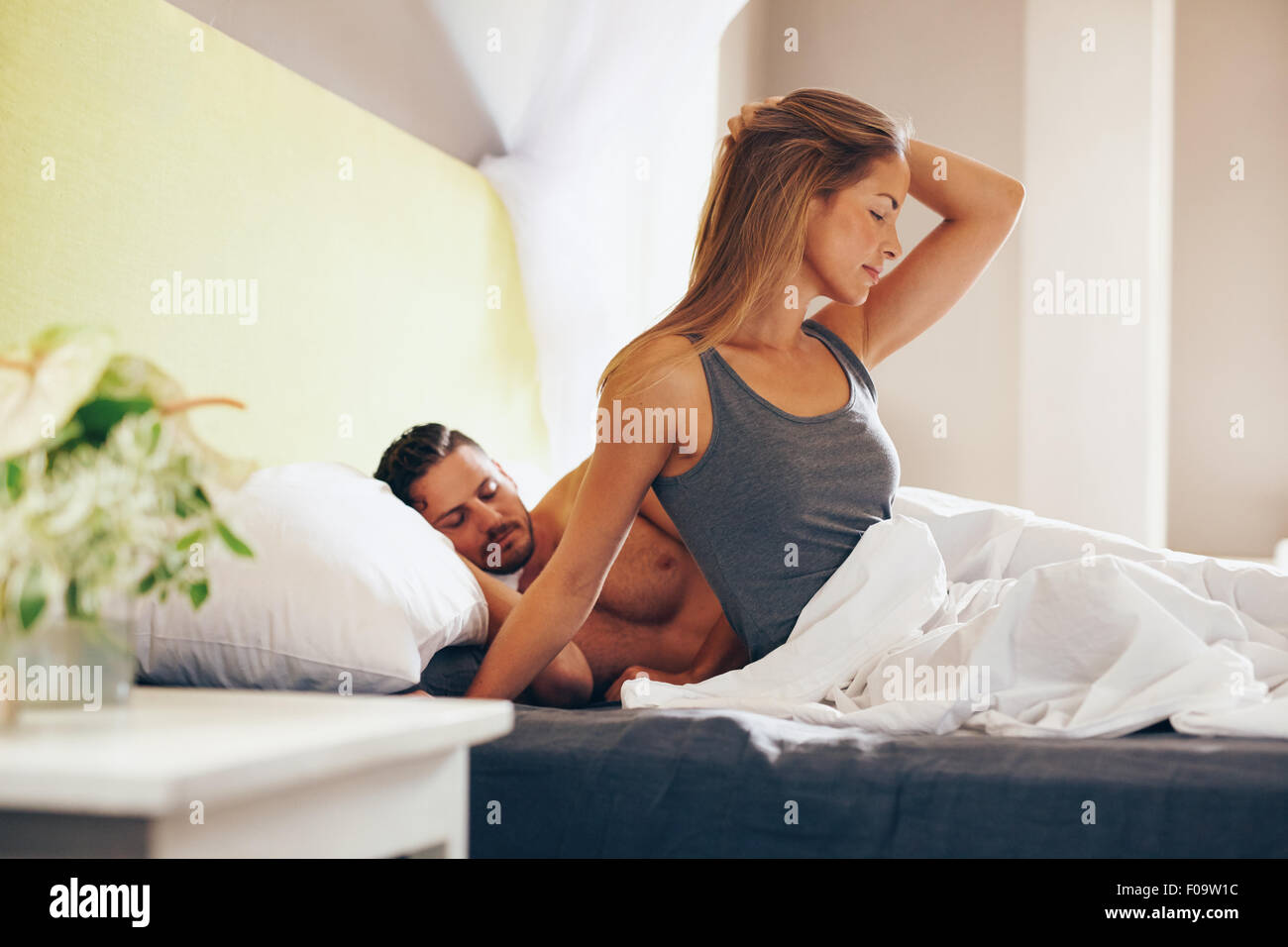 Porträt der attraktive junge Frau mit ihrem Mann schlafen hinter ihr morgens aufwachen. Kaukasische Frau sitzt am Bett Witz Stockfoto