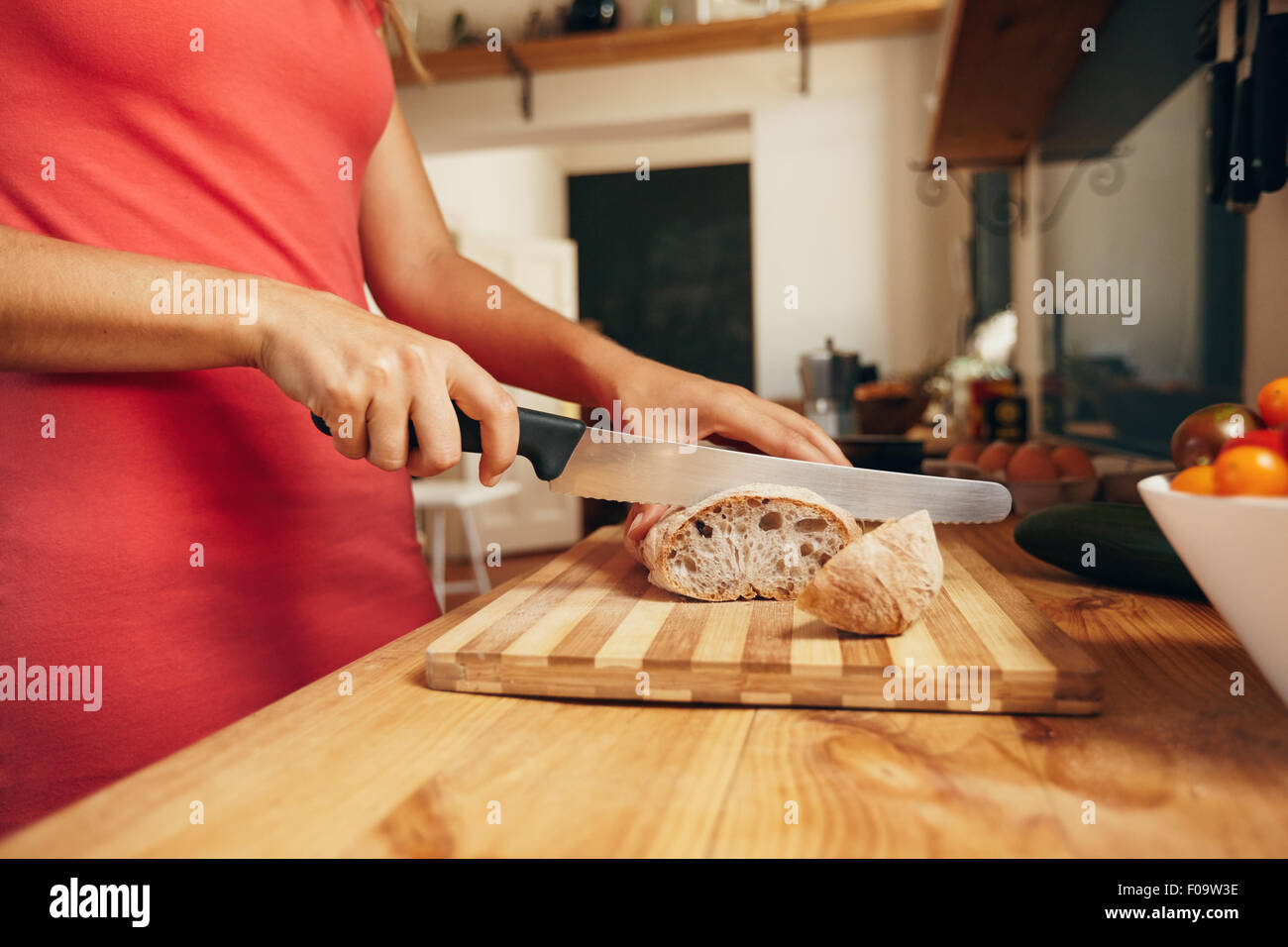 Frau Brot auf Schneidebrett mit Küchenmesser schneiden. Nahaufnahme der weiblichen Hände schneiden von Brot auf Küchentisch, Stockfoto