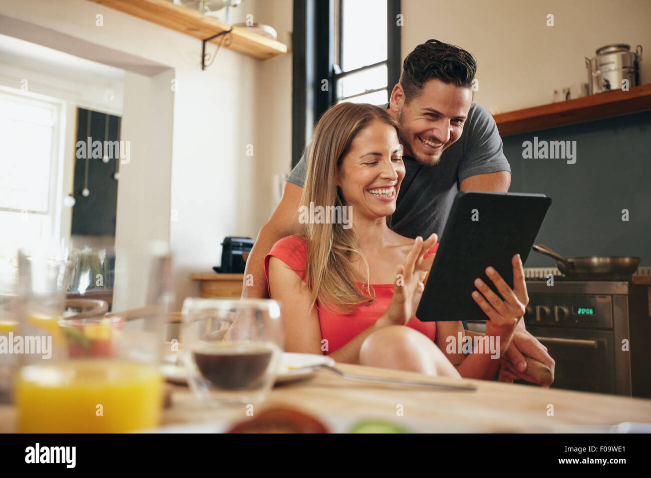 Glückliches junges Paar in der modernen Küche am Morgen mit einem digitalen Tablet. Lächelnde junge Frau zeigen etwas auf ihr bo Stockfoto