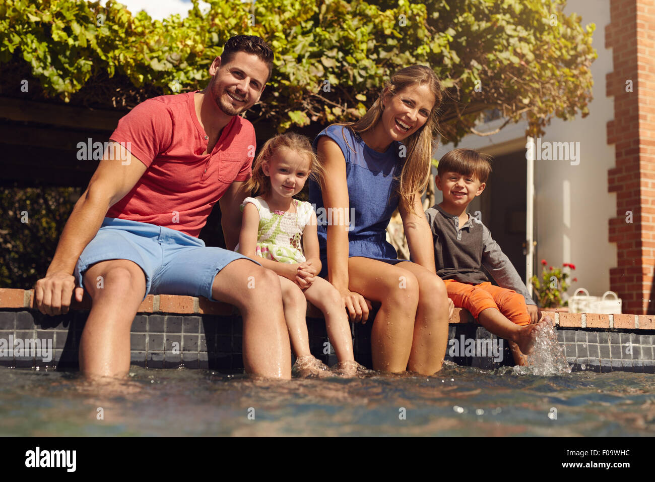 Familie mit Füßen im Pool sitzen. Junge Familie von vier sitzen am Rand  ihrer Pool Blick in die Kamera an einem sonnigen Tag Stockfotografie - Alamy