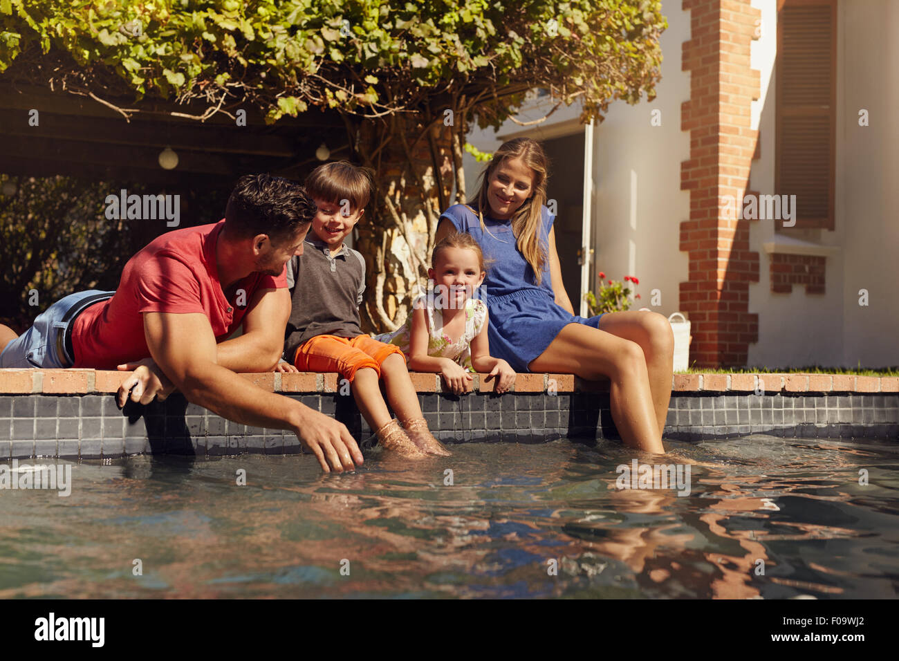 Porträt der jungen Familie mit zwei Kindern, die von ihrem Pool Spaß entspannend. Eltern mit Kinder sitzen auf dem Rand des Stockfoto