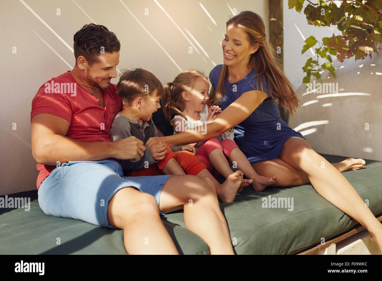 Schuss der glückliche junge Familie Zusammensitzen im Patio. Paar mit ihren Kindern sitzen auf der Couch im Hinterhof Spaß. Stockfoto