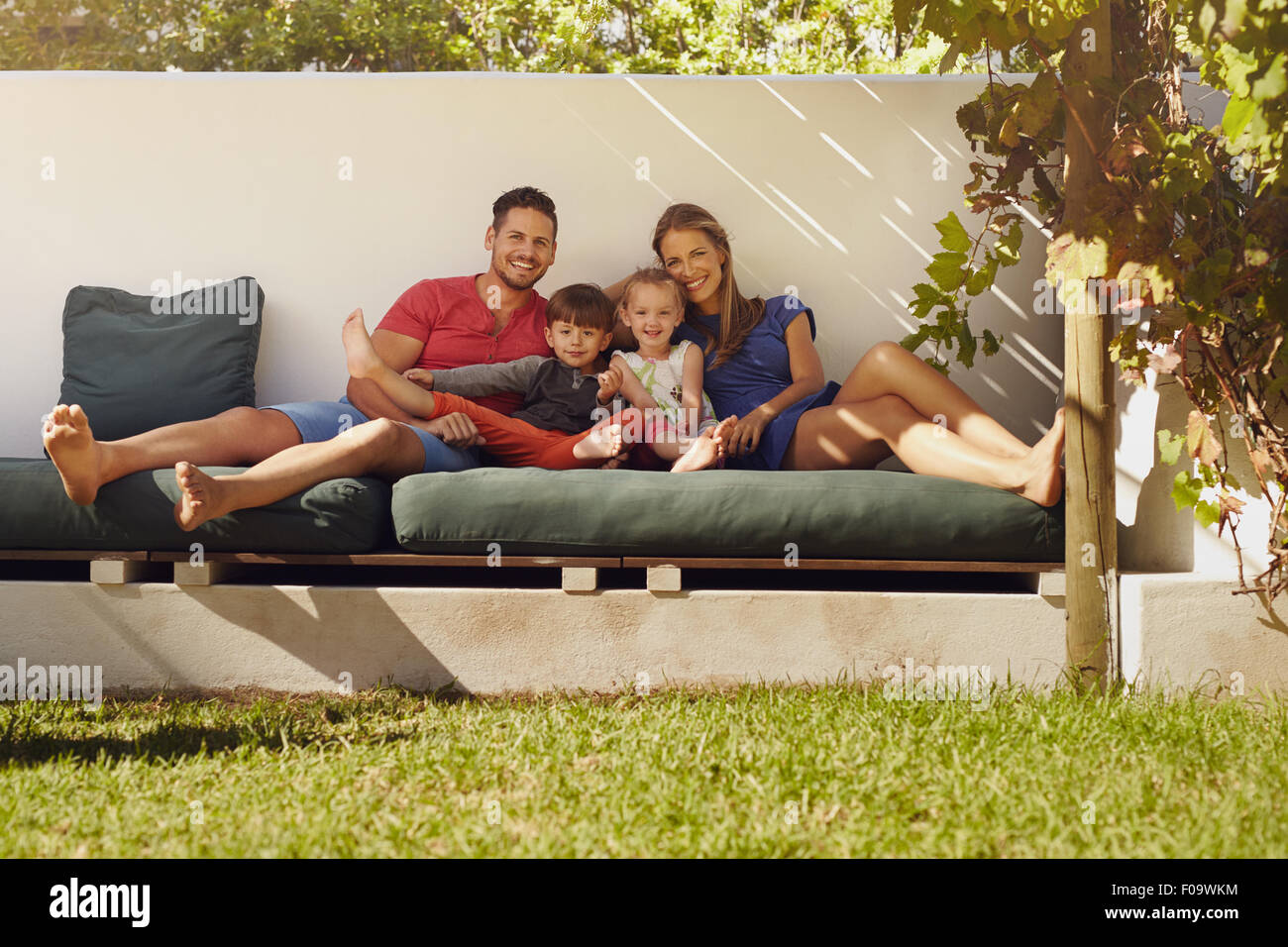 Porträt des jungen Familienglück sitzen auf der Terrasse in die Kamera Lächeln. Paar mit Kinder sitzen auf der Couch in ihrem Hinterhof. Stockfoto