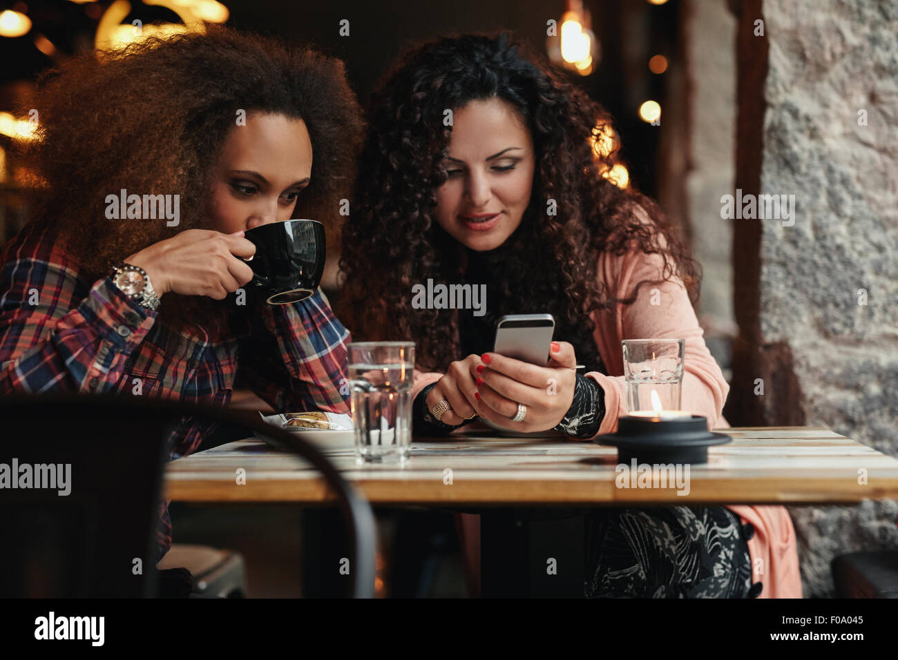 Junge Freunde sitzen in einem Café, ein Smartphone zu betrachten. Eine Frau Kaffee trinken und ein anderes Mobiltelefon zu halten, Stockfoto