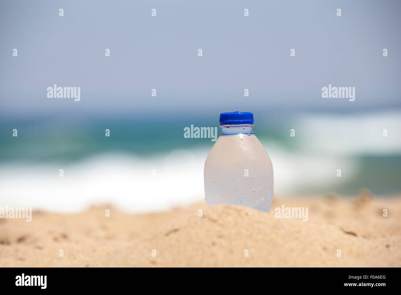 Verschwitzten Flasche mit kaltem Mineralwasser am Strand. Die Flasche wird verschlossen und auf dem Sand stehen. Es ist halb sichtbar auf einem ba Stockfoto