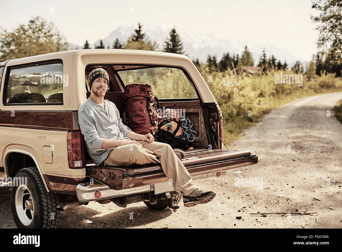 Junger Mann sitzt auf Rückseite des Pickup-Truck, Blick in die Kamera, Lächeln Stockfoto