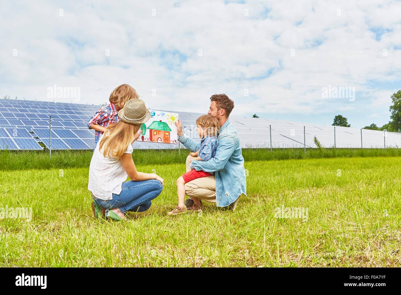 Junge Familie im Feld sitzen, mit Blick auf Kinder Zeichnung des Hauses, neben Solarpark Stockfoto