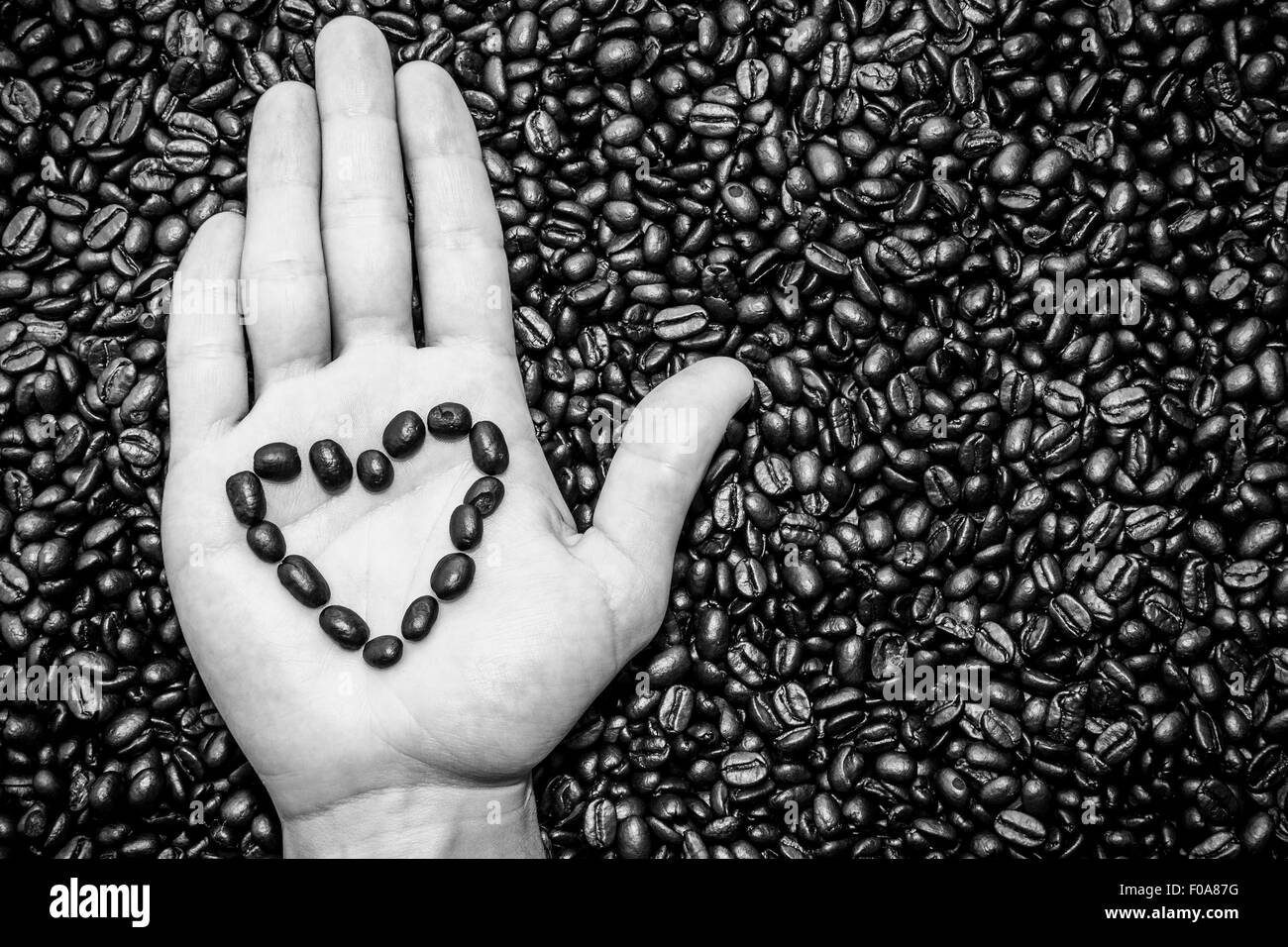 Kaffeebohnen-Herz-Symbol oben auf der Hand. Kaffeebohnen Textur unter. Stockfoto