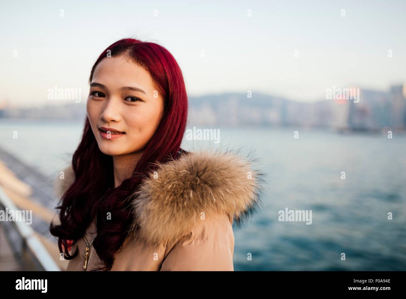 Porträt der jungen Frau mit Fell Trimmen Mantel mit gefärbten roten Haaren vor Wasser Stockfoto