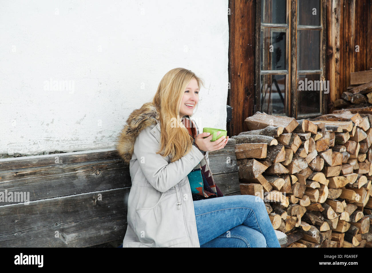 Junge Frau sitzt außerhalb Holzhütte Kaffeetrinken Stockfoto