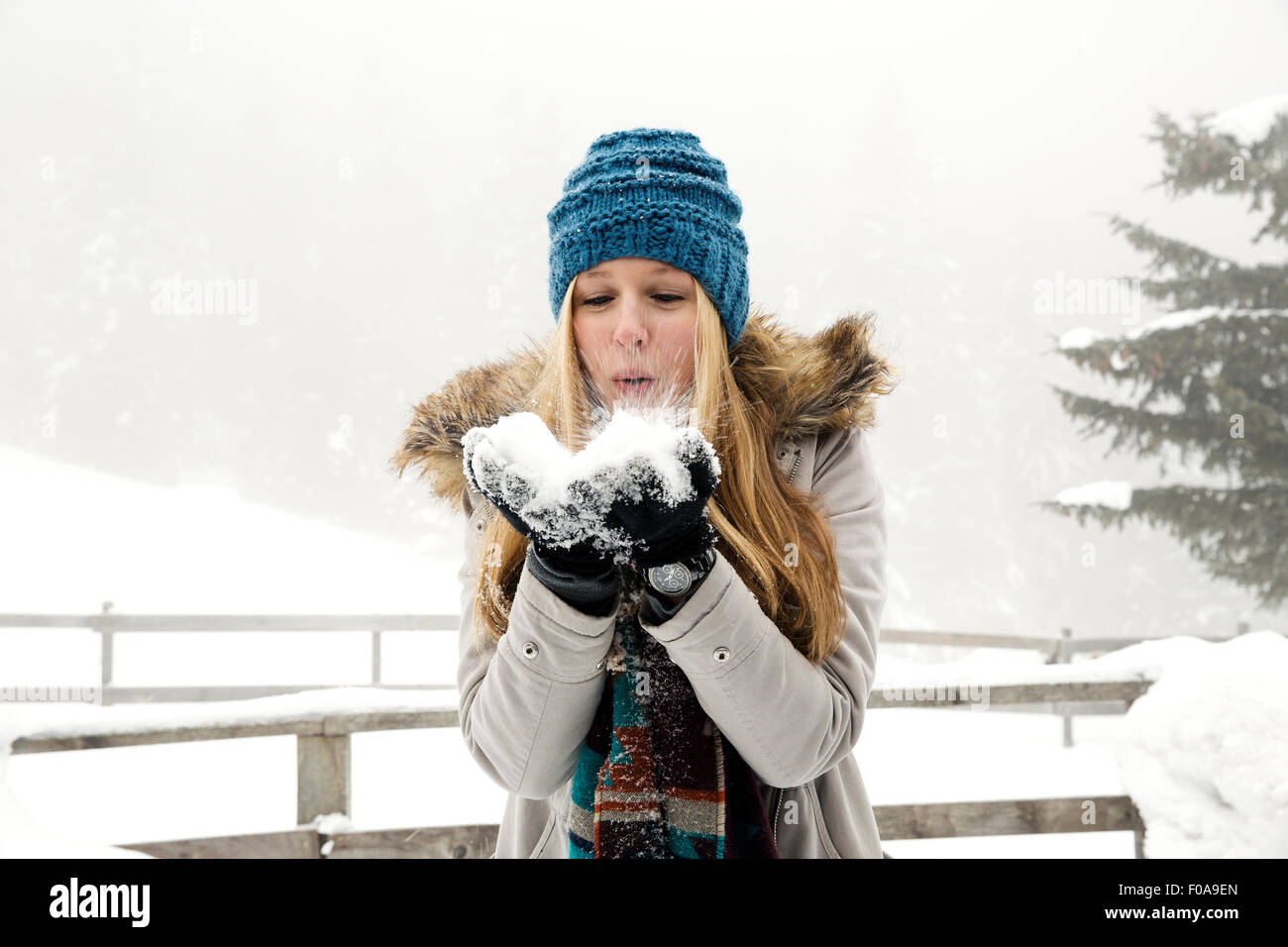Junge Frau bläst Handvoll Schnee Stockfoto