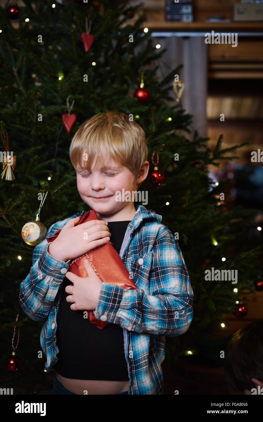 Junge hält Weihnachtsgeschenk mit geschlossenen Augen und Hoffnung Stockfoto