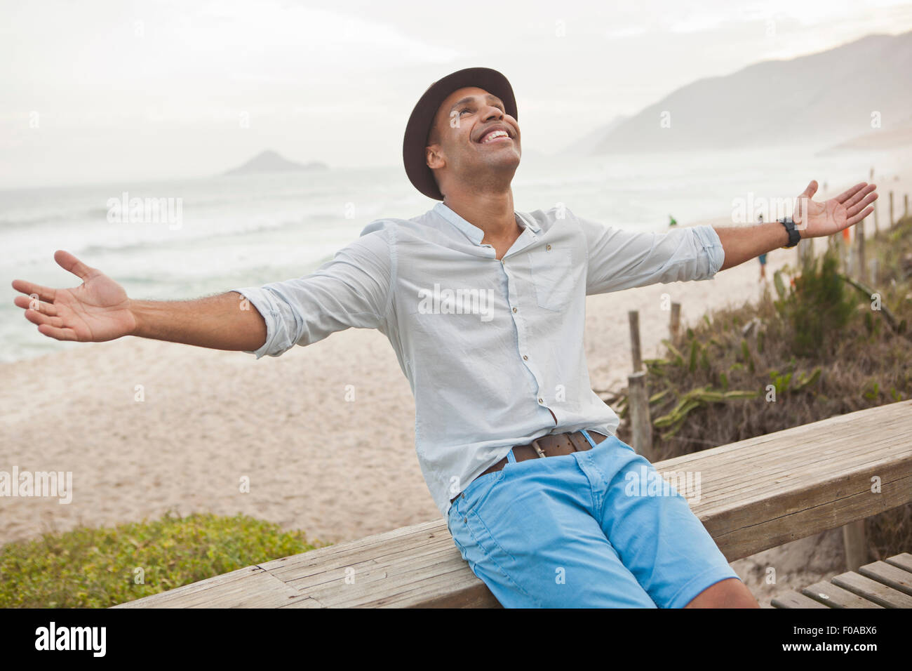 Mitte erwachsenen Mann sitzt auf Promenade Zaun mit Armen offen, Rio De Janeiro, Brasilien Stockfoto