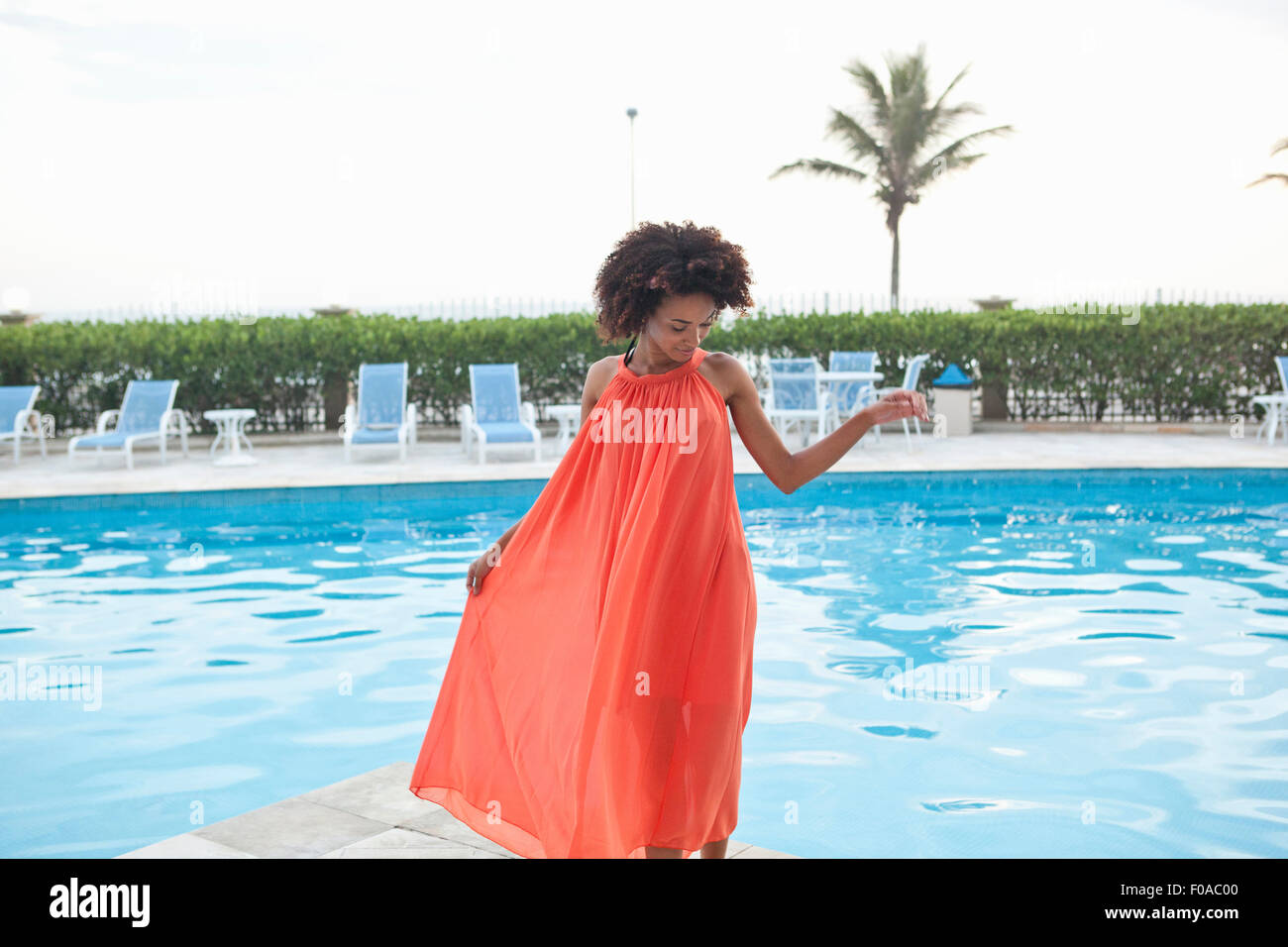 Junge Frau trägt orange Kleid am Hotel Pool, Rio De Janeiro, Brasilien Stockfoto