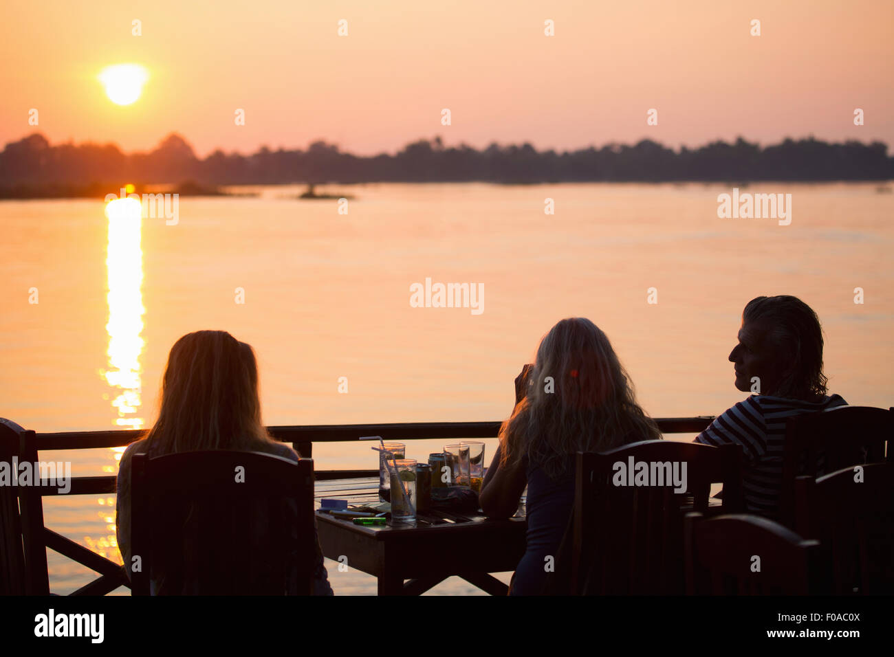 Rückansicht von drei Erwachsenen Freunden Sonnenuntergang über dem Mekong-Fluss, Don Det, Laos Stockfoto