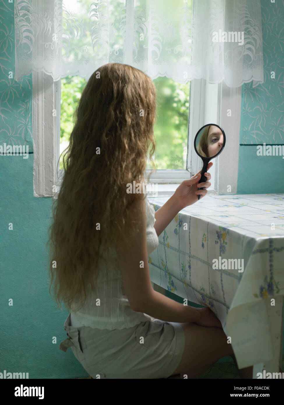 Reflexion der jungen Frau, die in der hand Spiegel in Küche Stockfoto