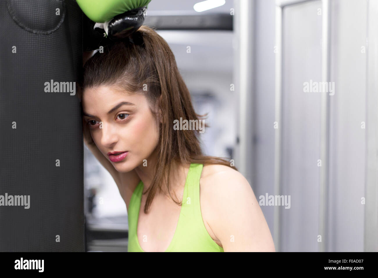 Porträt einer jungen Frau im Fitnessstudio tragen Boxhandschuh Boxsack gelehnt Stockfoto