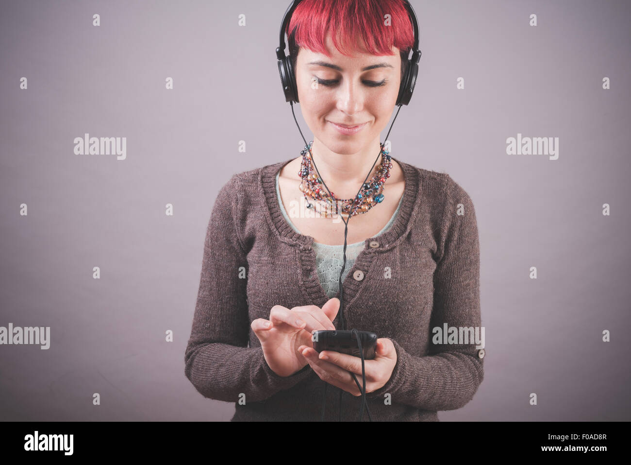 Studio-Porträt der jungen Frau mit kurzen rosa Haaren Auswahl Musik auf smartphone Stockfoto