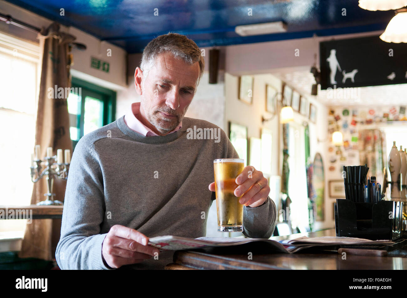Reifer Mann trinkt Bier und liest Zeitung im pub Stockfoto