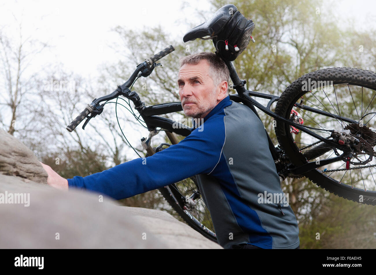 Ältere männliche Biker tragen Mountainbike über Felsformation Stockfoto