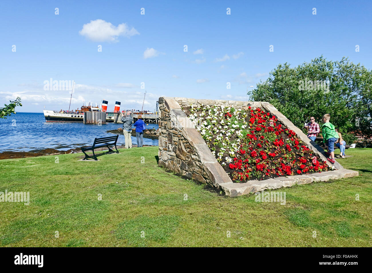 Die Strandpromenade von Brodick in Arran Schottland mit erhöhten Blumenbeet und Paddel-Dampfer Waverley am Pier. Stockfoto