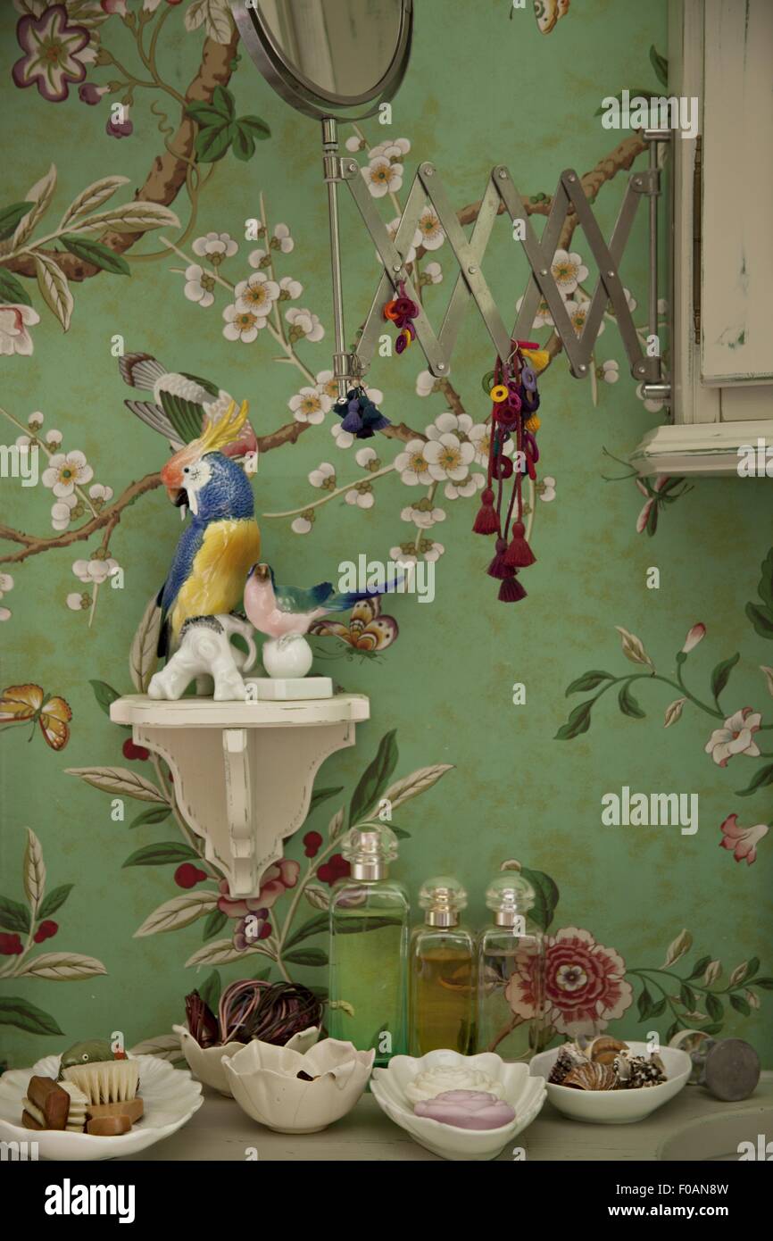 Tapete mit floralen Motiv, Papagei, Keramik, Konsole und Eitelkeit Spiegel gegen grüne Wand Stockfoto