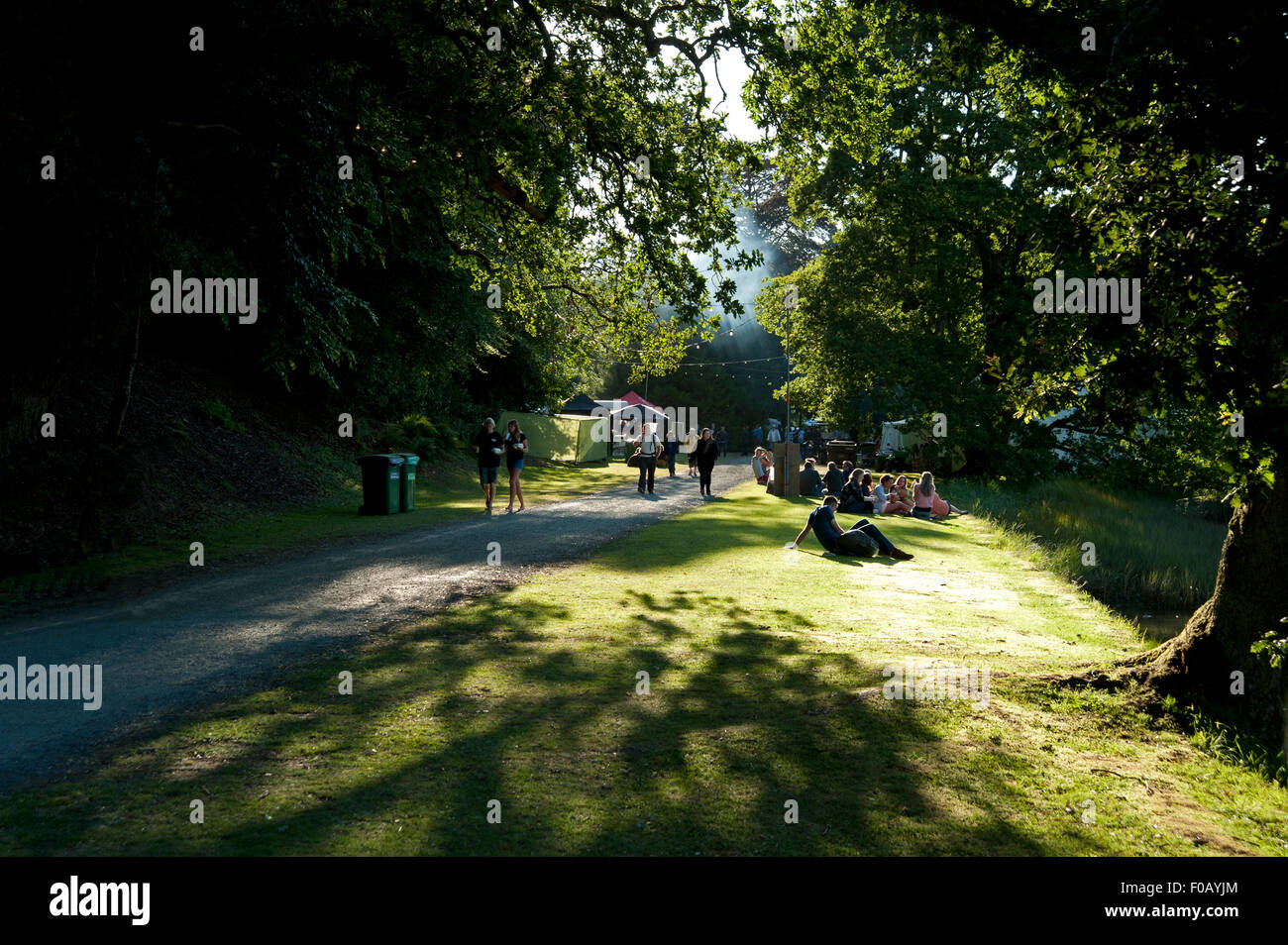 Festivalbesucher Spaziergang durch die Bäume mit der Sonne glitzert auf dem Rasen auf dem Port Eliot Festival in Cornwall Stockfoto