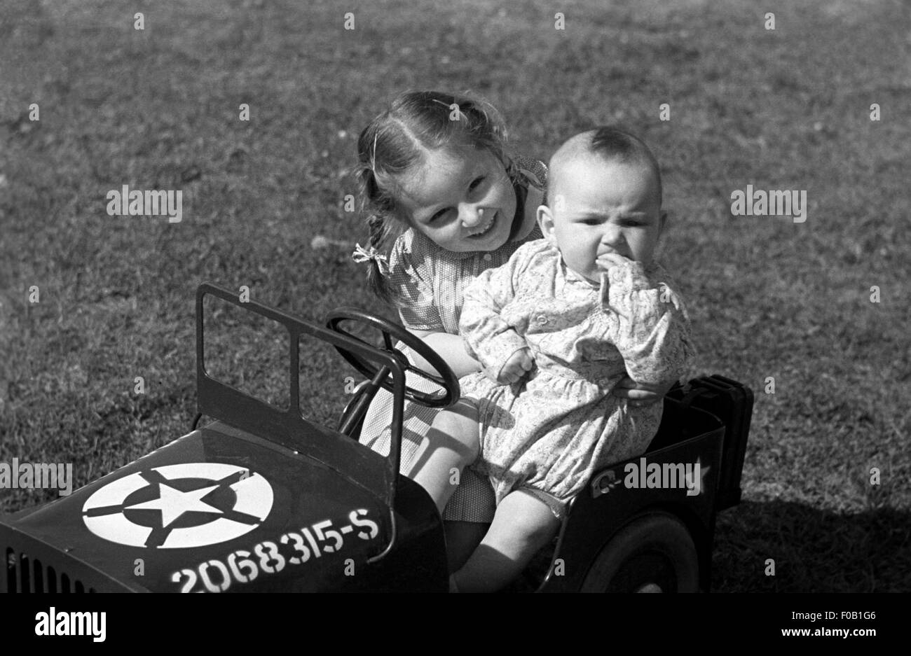 Porträt eines jungen Mädchens mit Babyschwester sitzt in einem Spielzeug amerikanischen jeep Stockfoto
