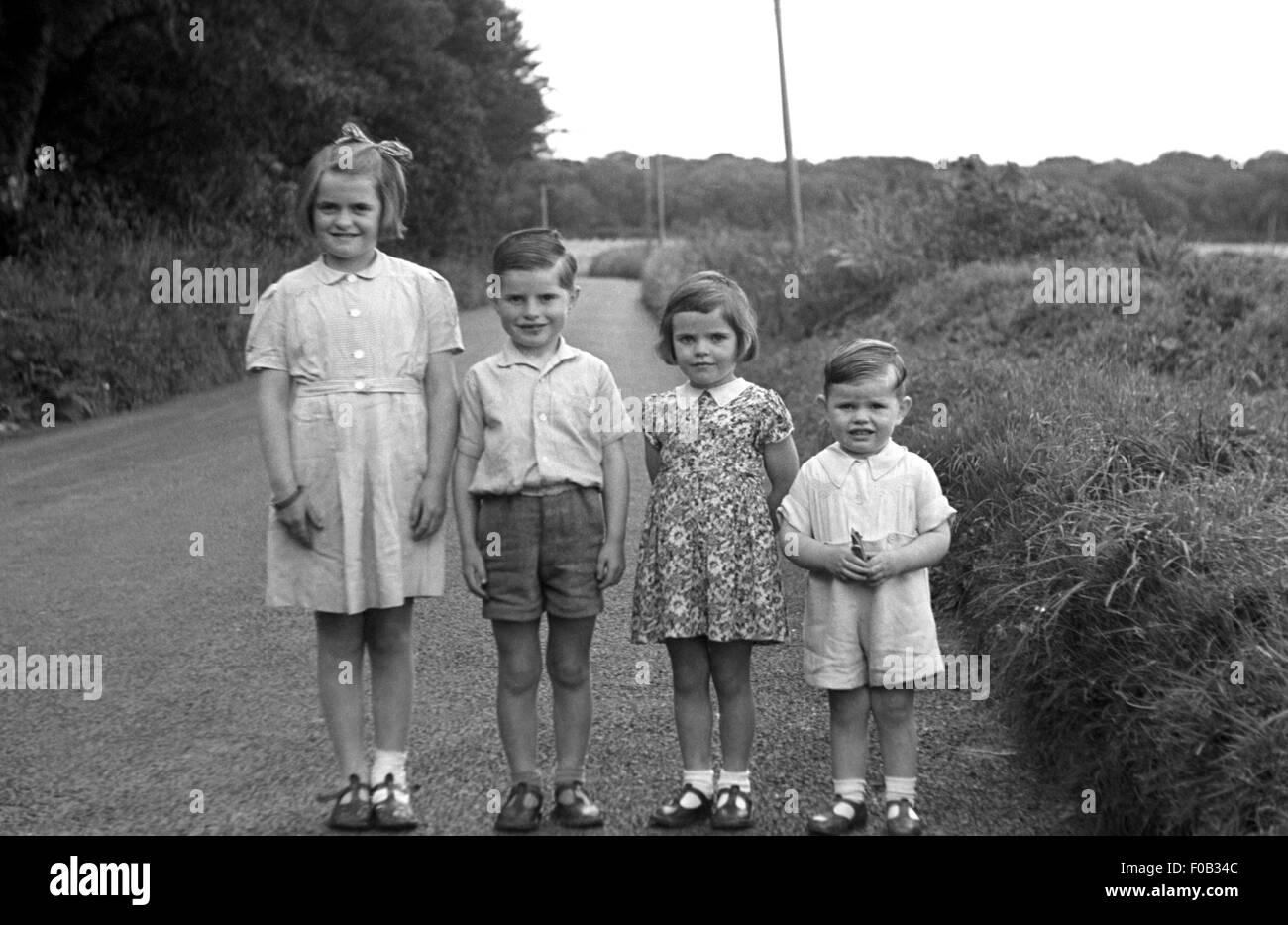 Vier kleine Kinder stehen in der Reihenfolge der Höhe auf einer Landstraße. Stockfoto