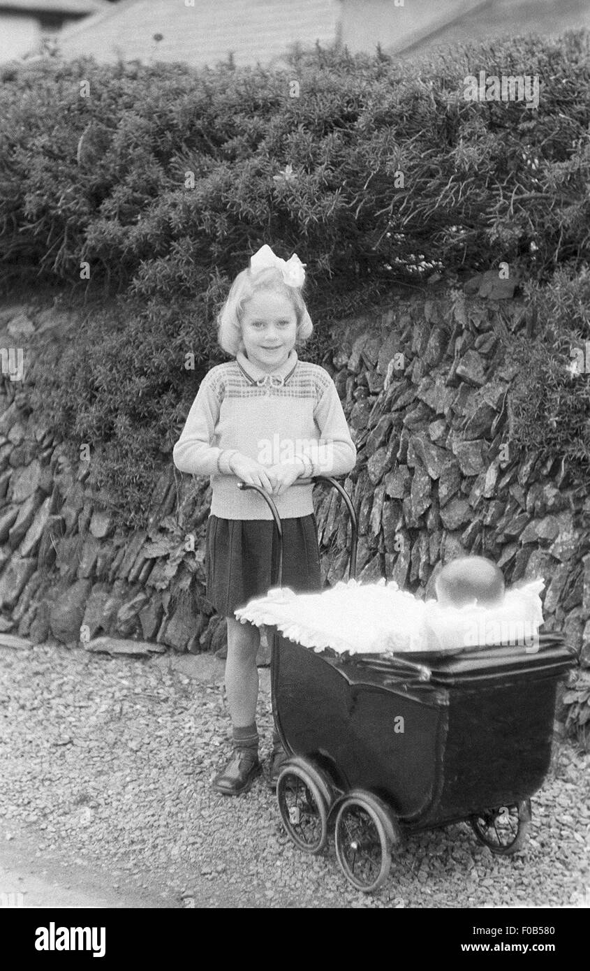 Ein junges Mädchen mit ihren Puppen Kinderwagen im Garten Stockfoto
