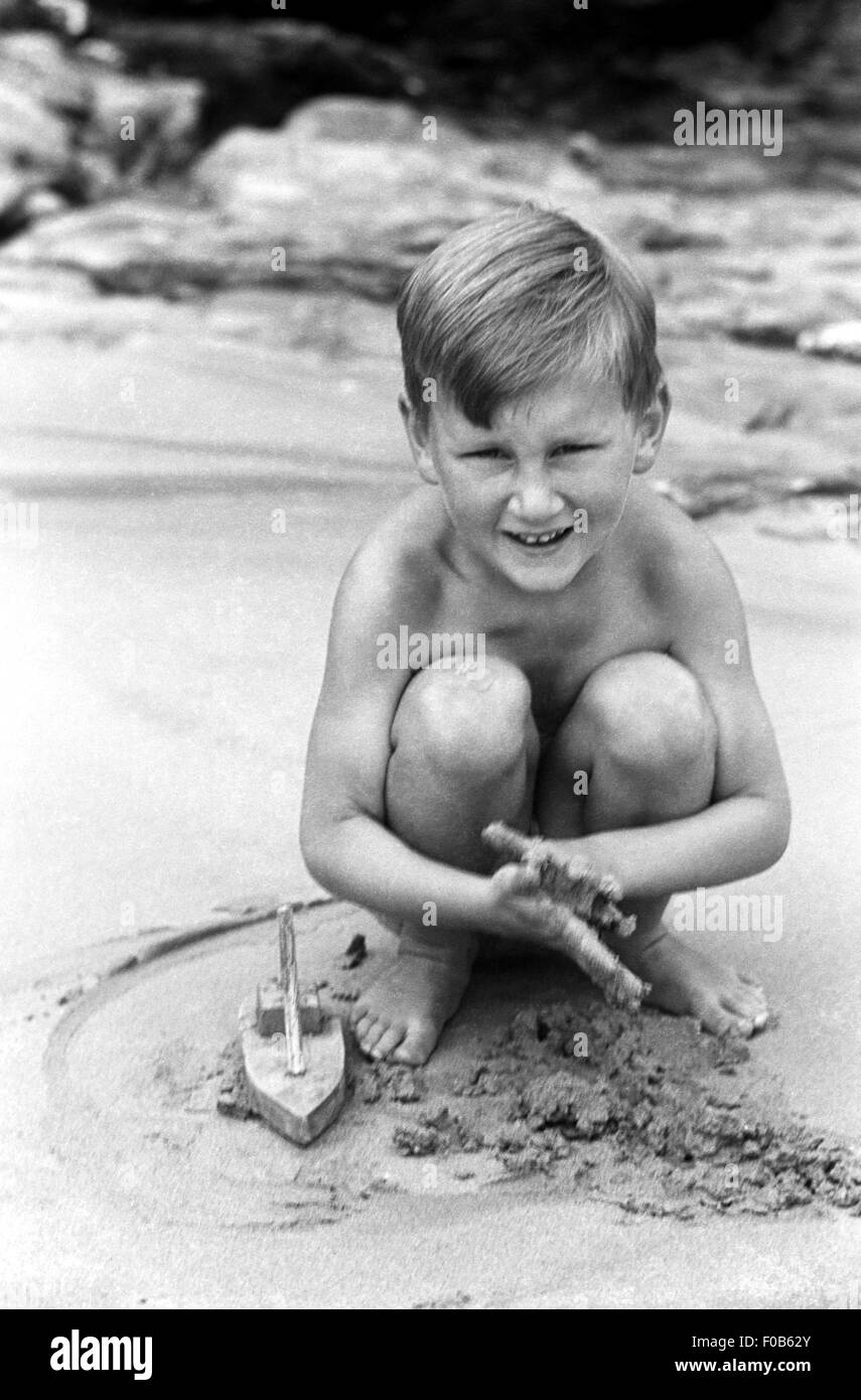 Ein fair haired junge spielt in den Sand mit einem Spielzeug Holzboot Stockfoto