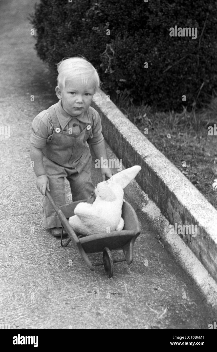 Ein kleiner Junge mit seinem Spielzeug-Kaninchen in eine Schubkarre. Stockfoto