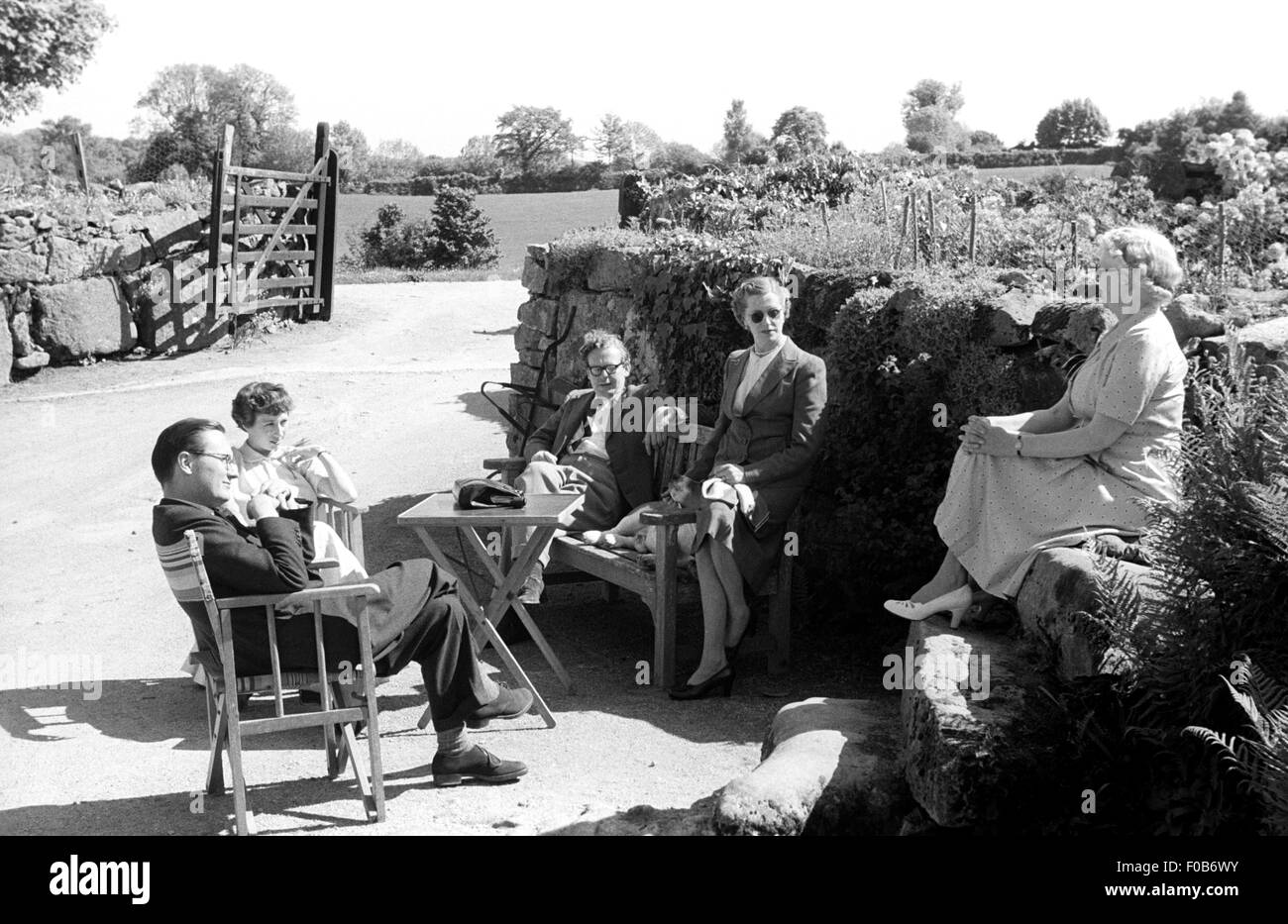 Eine Gruppe von elegant gekleideten Menschen draußen in einem Garten von einem Haus auf dem Land. Stockfoto
