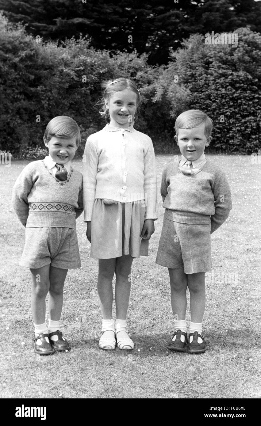 Drei elegant gekleidete Kinder stehen in einem Garten. Stockfoto