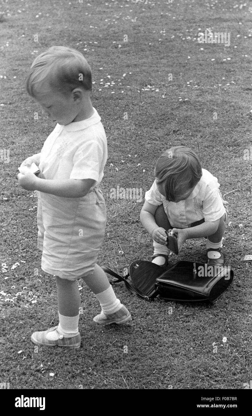 Zwei jungen auf der Suche auf den Inhalt von einer Frau die Handtasche auf dem Rasen im Garten. Stockfoto