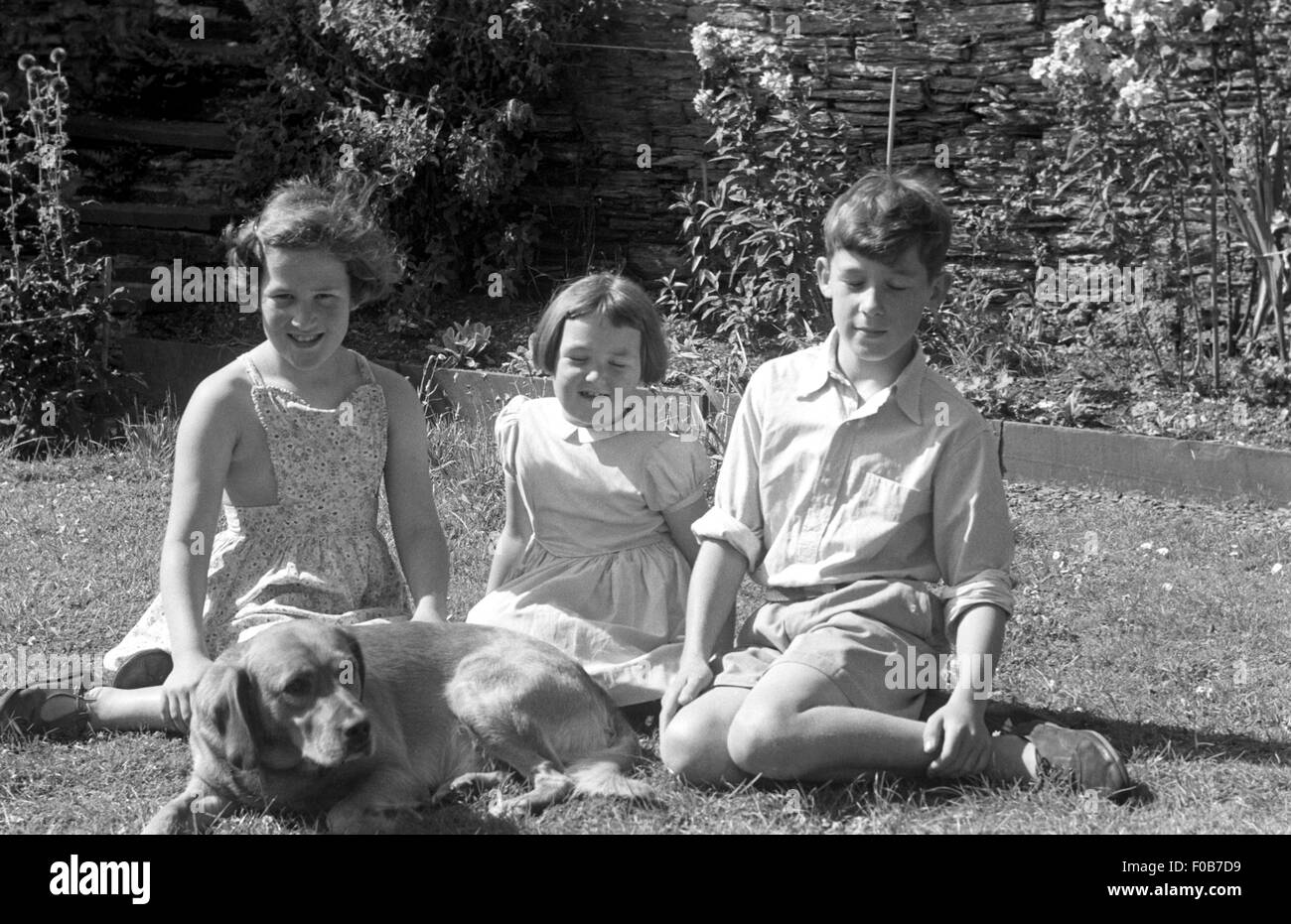 Zwei Mädchen und ein Teenager sitzen auf dem Rasen im Garten Stockfoto