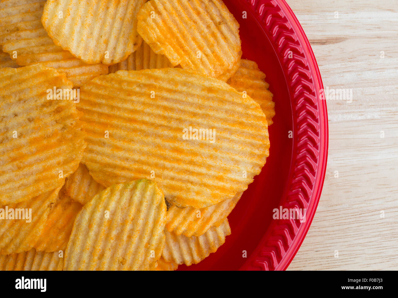 Enge Draufsicht Cheddar Käse gewürzt Kartoffelchips auf einer roten Plastikschale auf einer hölzernen Tischplatte durch natürliches Licht beleuchtet. Stockfoto