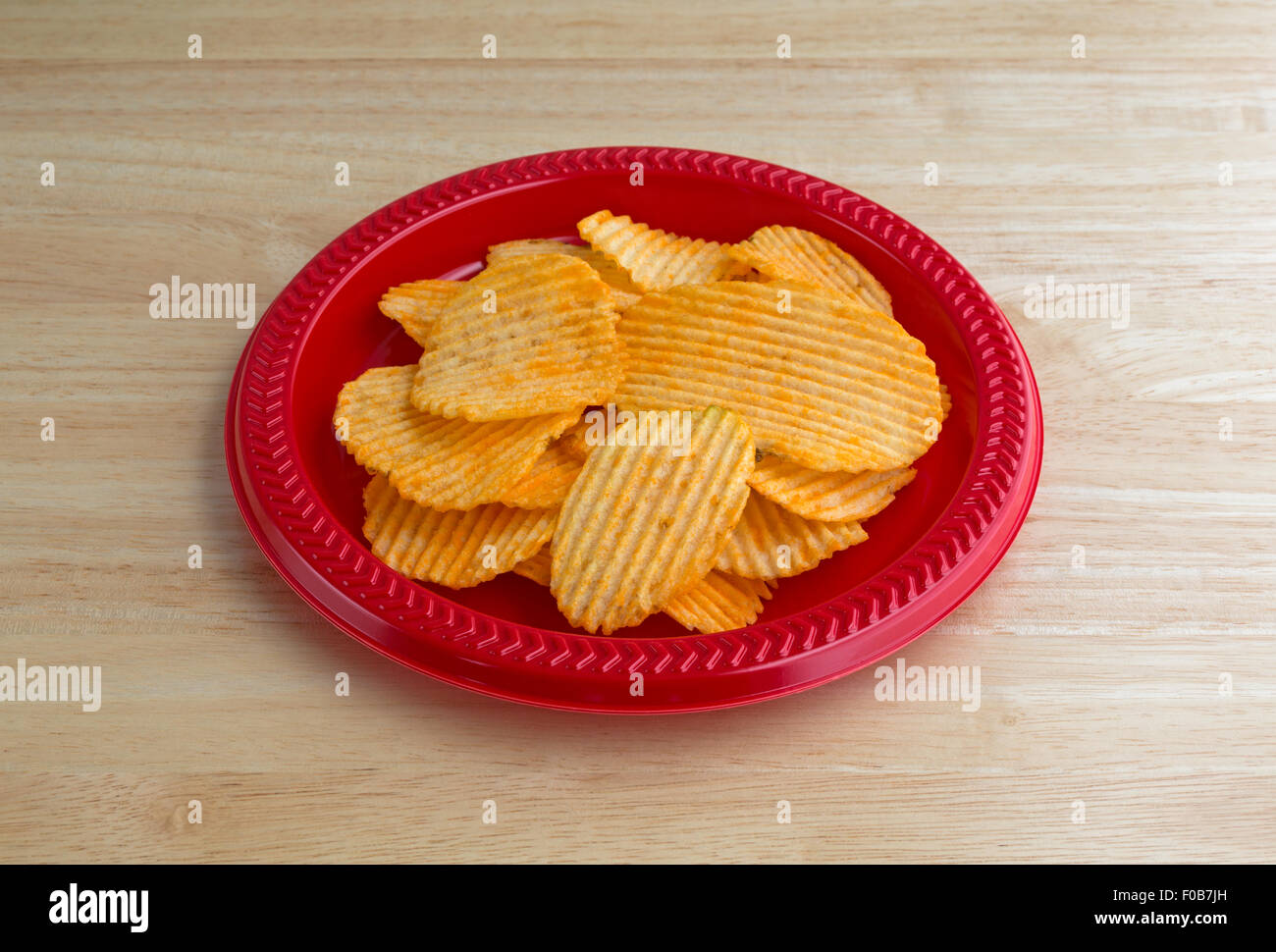 Eine rote Kunststoffplatte mit einer Portion Cheddar Käse gewürzt Kartoffelchips auf einer hölzernen Tischplatte mit natürlichem Licht beleuchtet. Stockfoto