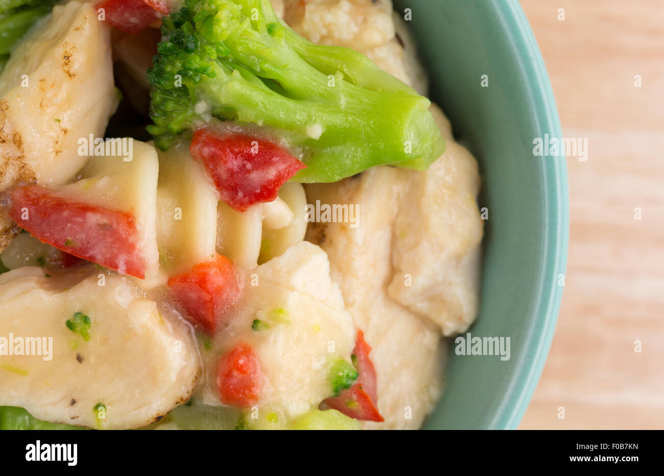Enge Draufsicht einer Portion gegrilltes Huhn mit verschiedene Gemüse in einer Knoblauchsauce in einer Schüssel auf einer hölzernen Tischplatte. Stockfoto