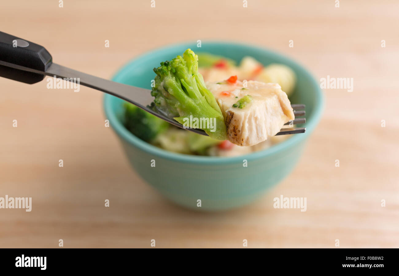 Nahaufnahme einer Gabel mit einem Stück von Broccoli und gegrilltes Hähnchen in Knoblauchsauce im Vordergrund Stockfoto