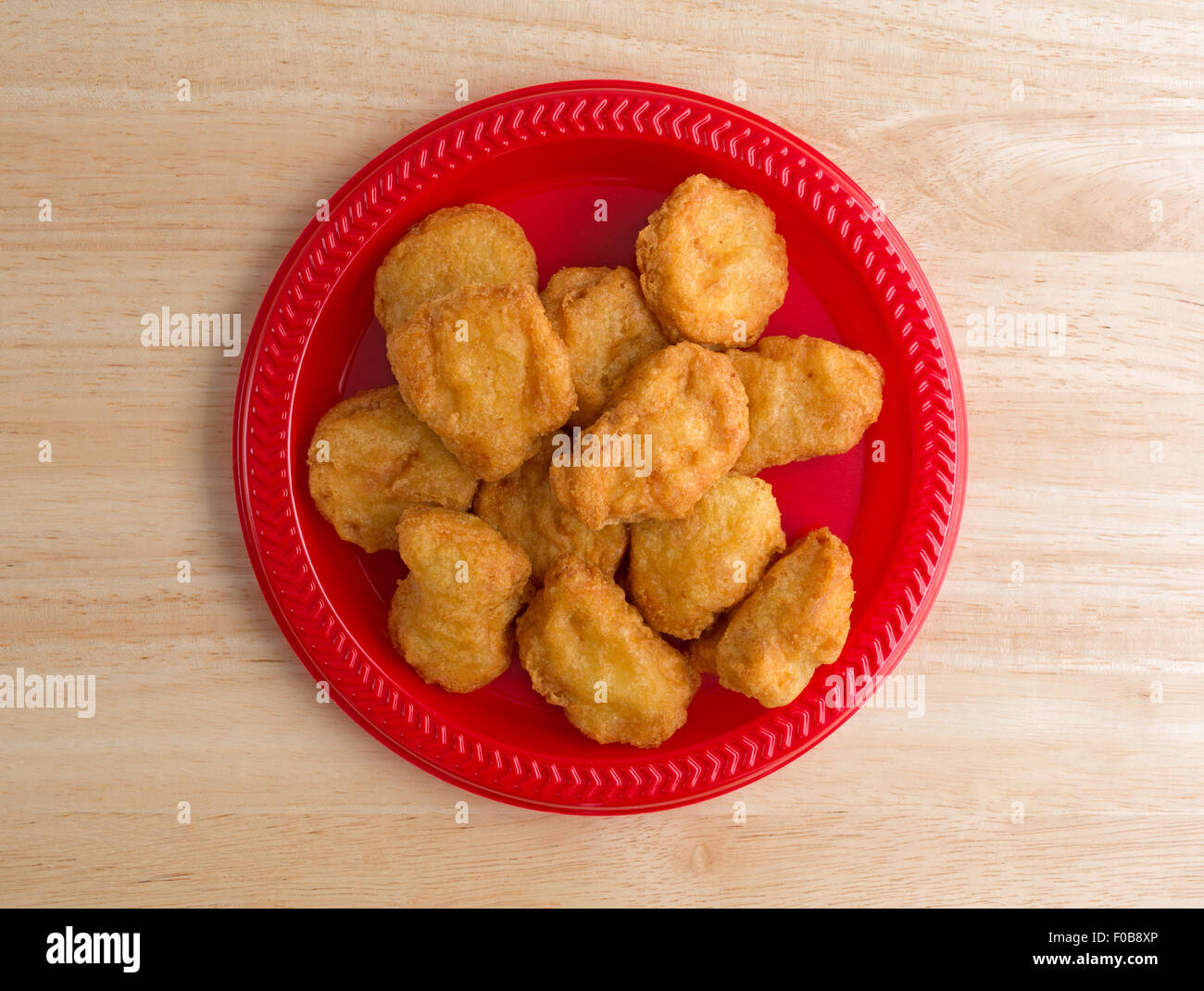 Draufsicht auf eine Portion Chicken Nuggets auf einer roten Platte auf einer hölzernen Tischplatte mit Fenster Licht beleuchtet. Stockfoto