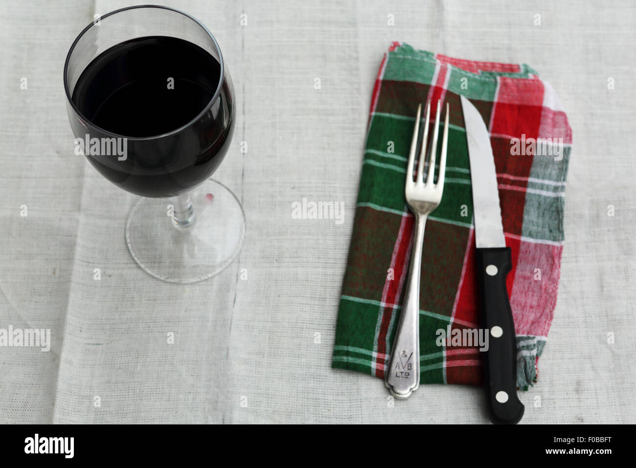 Ein Glas Rotwein wird am Tisch serviert. Eine Serviette mit Messer und Gabel steht neben dem Wein. Stockfoto
