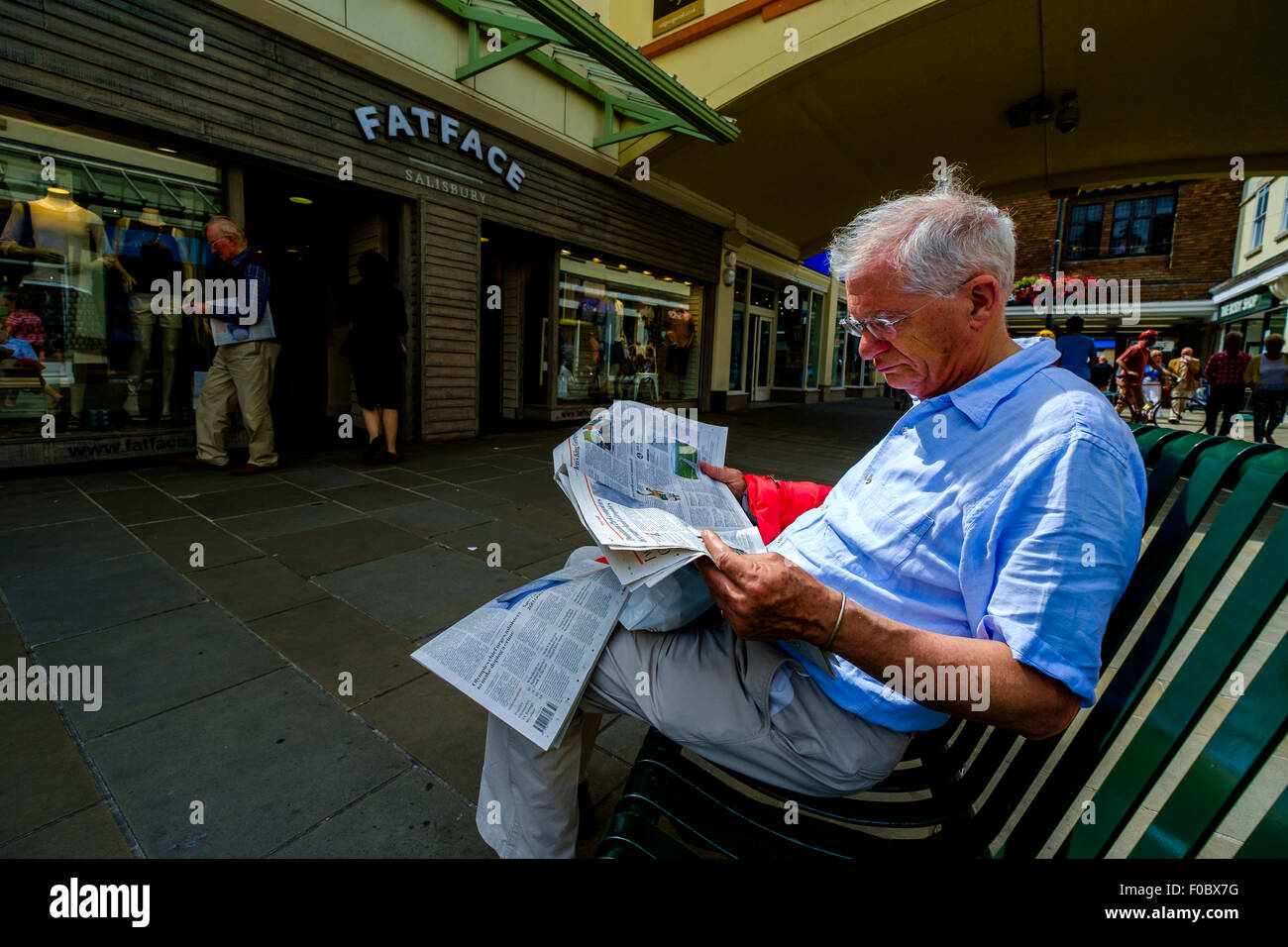 Männliche eine Zeitung lesen saß auf einer Bank im Einkaufszentrum Salisbury Wiltshire Stockfoto