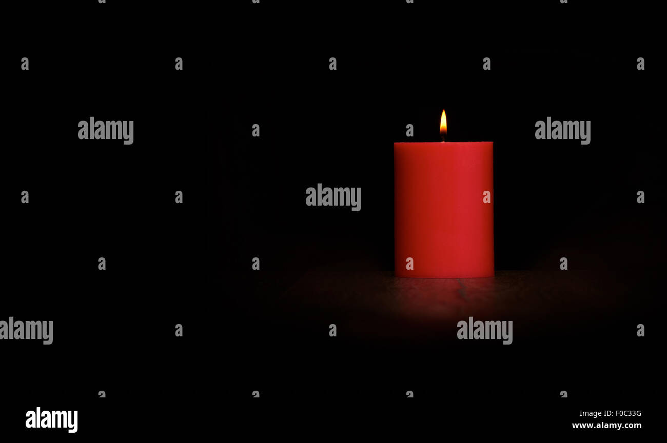 Brennende rote Kerze auf einem dunklen Holzboden mit schwarzem Hintergrund. Stockfoto